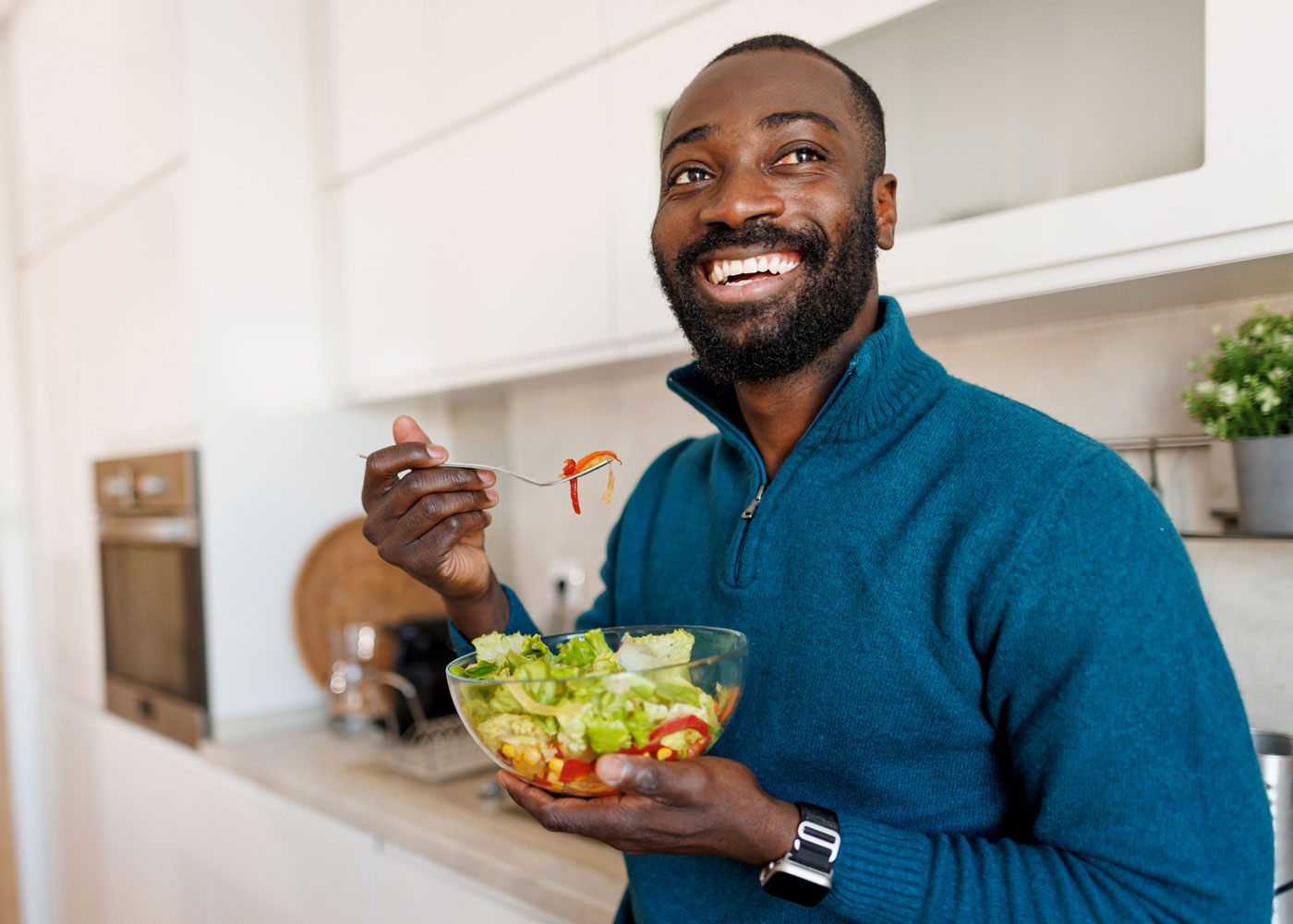 Male eating salad in a kitchen.